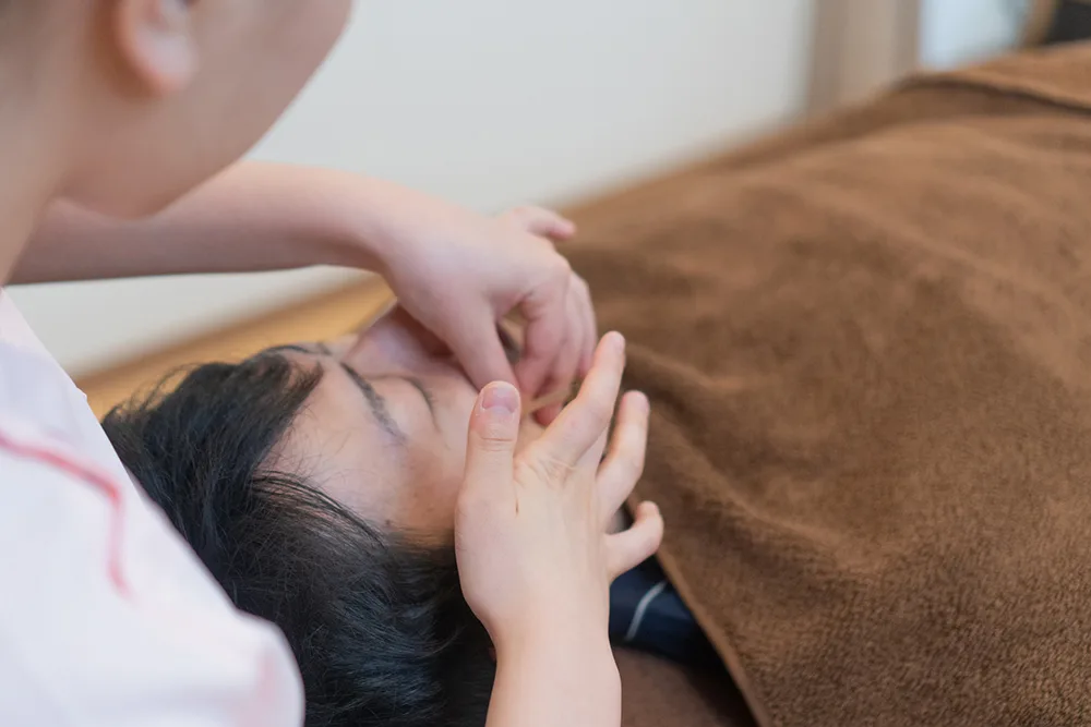 オムリス鍼灸接骨院でスタッフが仰向けの患者の首まわりを施術している様子