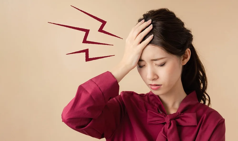 頭痛でお悩みの女性が頭を抱えている画像